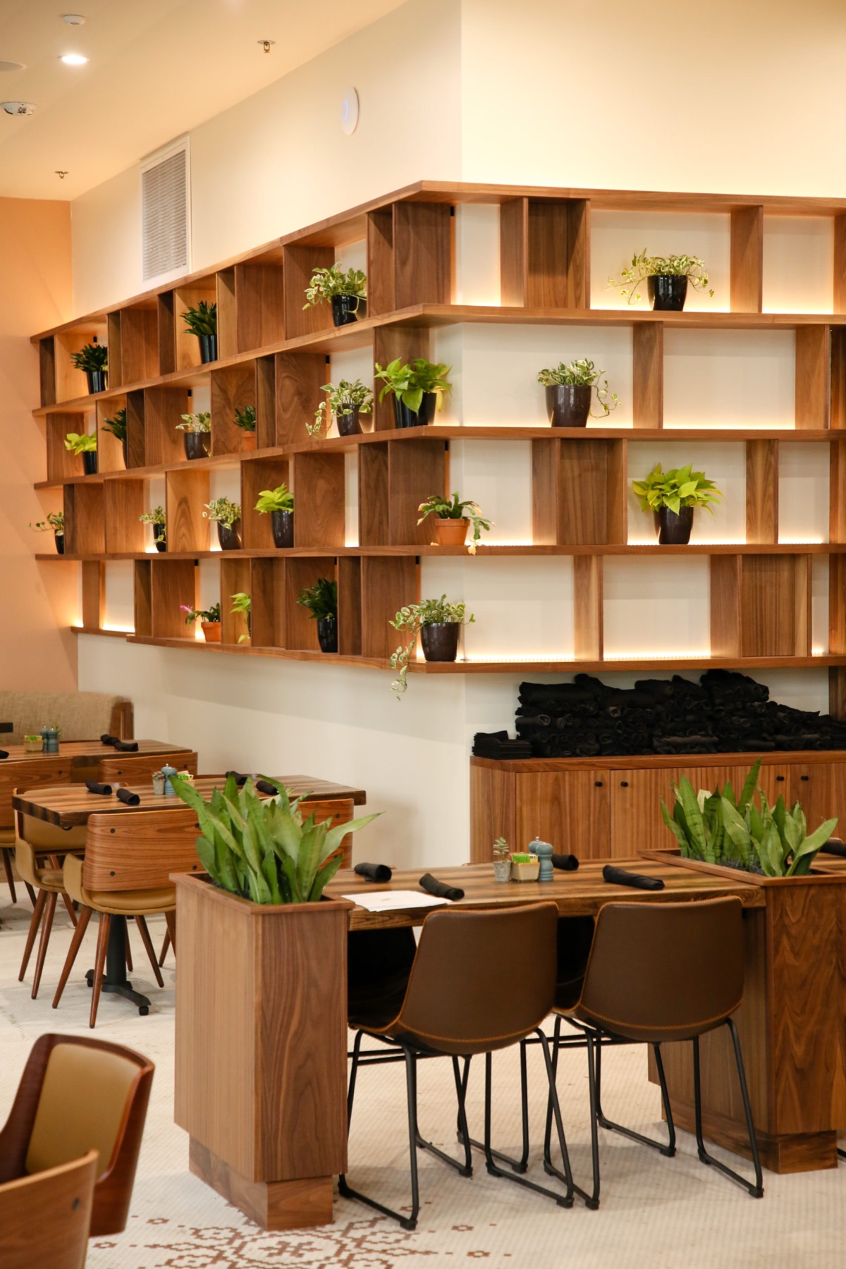 Restaurant with a lit walnut shelving wall and planter booths